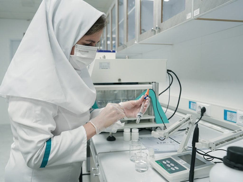 Laboratóriumi szakember védőfelszerelésben gyógyszeripari mintákat vizsgál a minőségellenőrző munkaasztalnál.